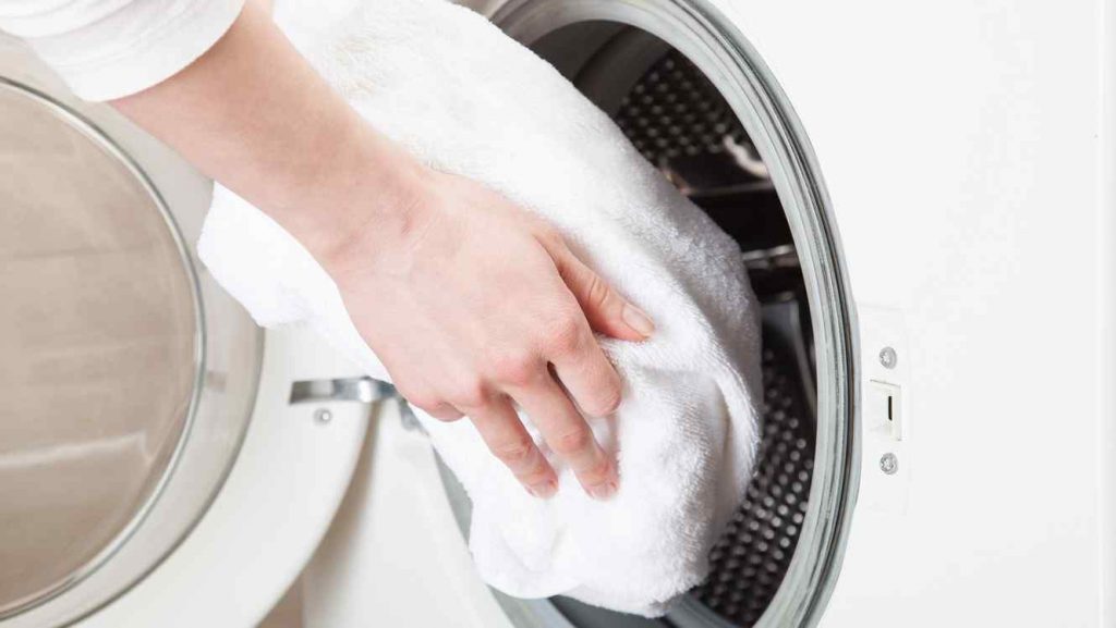 mujer colocando toallas blancas dentro de una lavadora